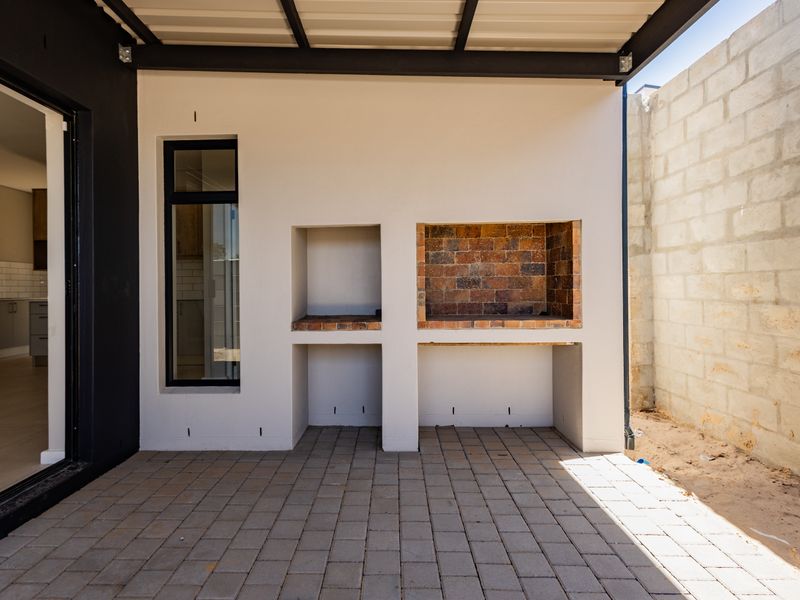 Covered patio area featuring a built-in brick braai, paved flooring, and direct access to the interior living space through a sliding door.