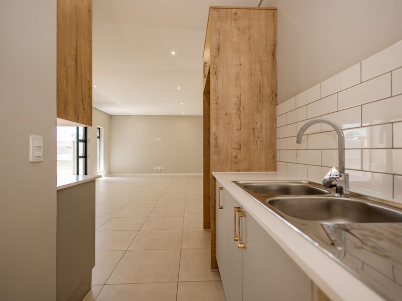 Modern open-plan living area featuring a sleek kitchen with wood-look cabinetry, subway tile backsplash, and a double bowl sink, flowing into a spacious living zone.