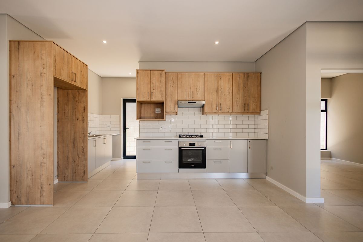 Modern kitchen featuring light wood-tone cabinetry, subway tile backsplash, built-in oven, gas hob, and neutral tiled flooring in an open-plan layout.
