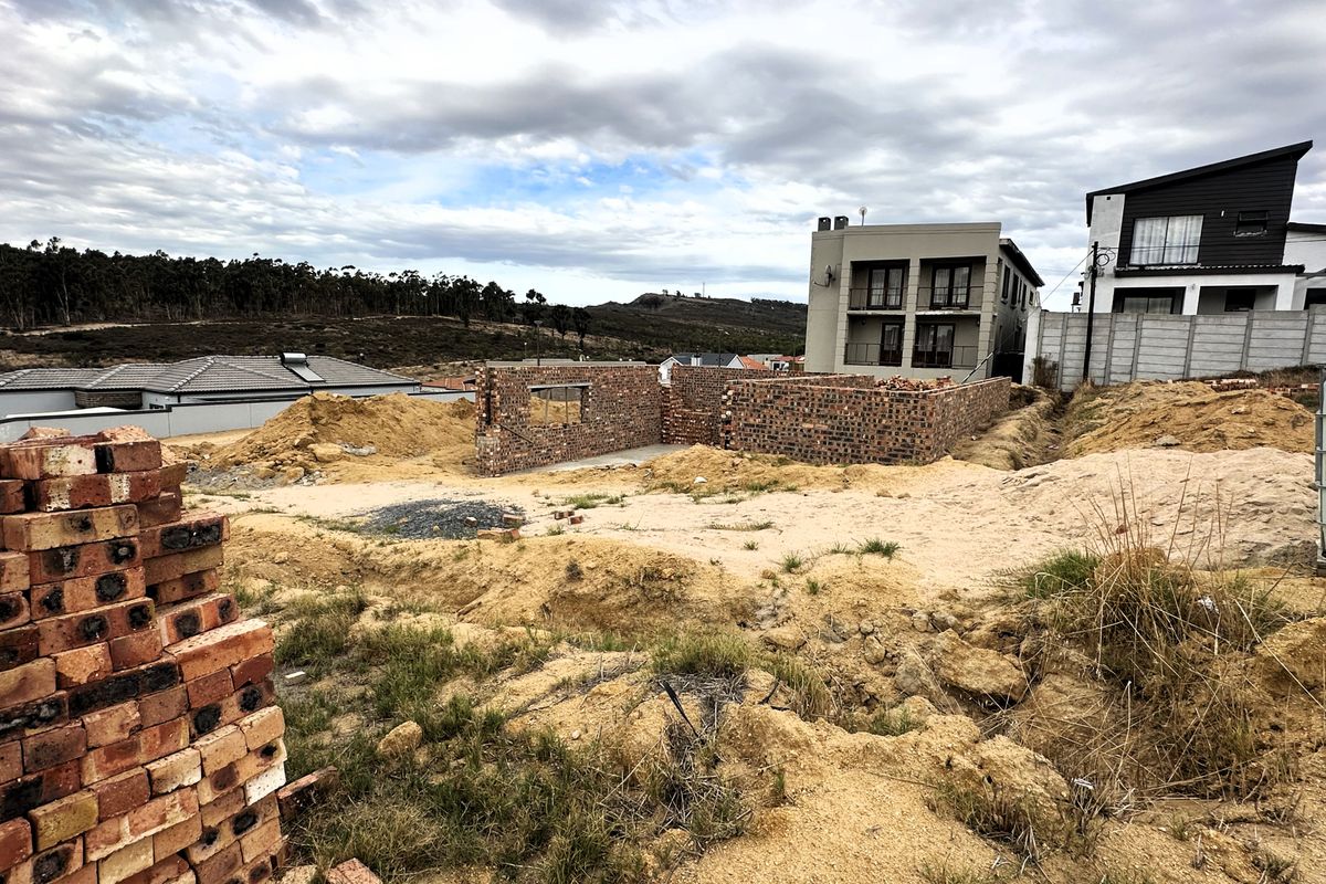 A vacant residential plot featuring partially constructed brick foundation walls, situated in a developing neighborhood with surrounding residential properties.
