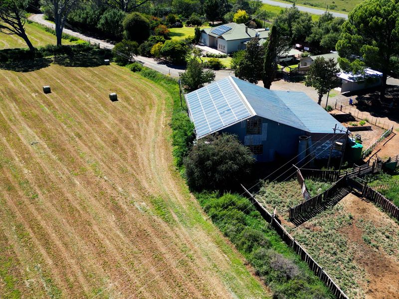 Aerial view of a farm property featuring a large shed with extensive roof-mounted solar panels, adjacent grazing fields, and fenced livestock enclosures.