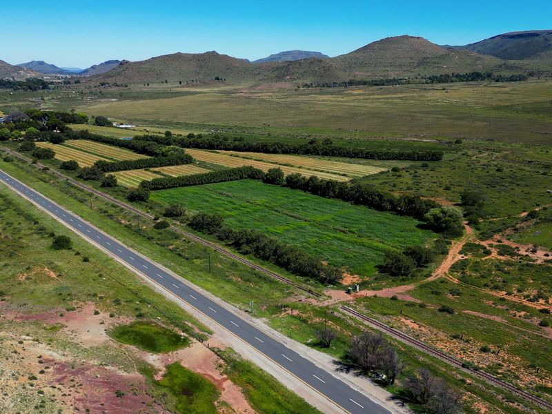 Aerial view of the farm property featuring expansive agricultural fields, adjacent road access, and scenic mountain landscape views.