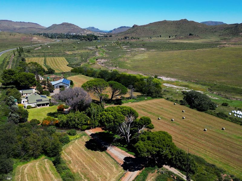 Aerial view of a rural farm property featuring agricultural fields, mature trees, and a main dwelling complex situated near a road.