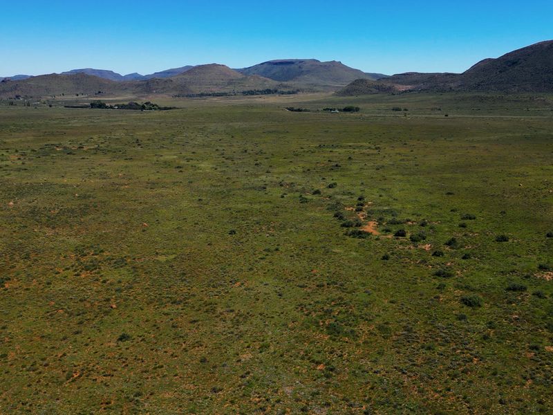 Expansive aerial view of the open farm landscape featuring rolling hills and natural vegetation under a clear blue sky.