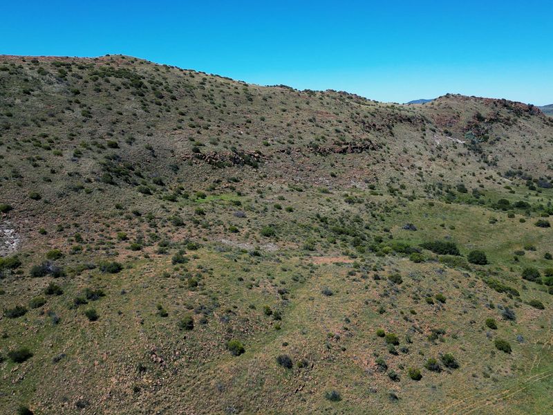 An expansive aerial view of the rugged, hilly landscape characteristic of the farm property, showcasing natural terrain and native vegetation.