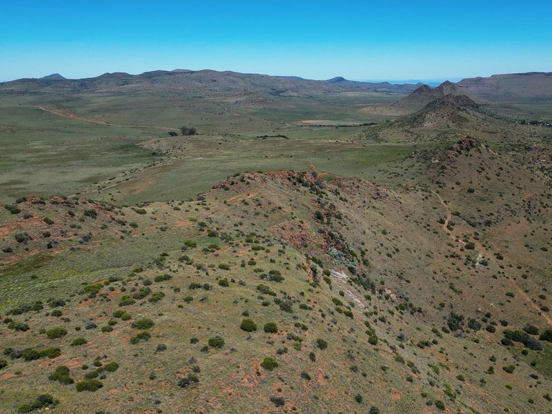 An expansive aerial view of the vast, rugged farm landscape featuring rolling hills, natural vegetation, and open terrain under a clear blue sky.
