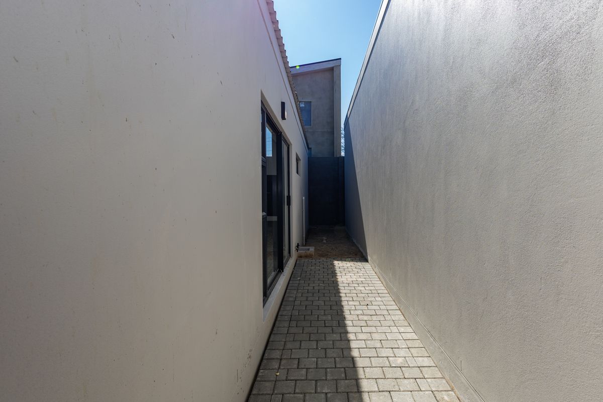 A narrow side passage featuring paved flooring and clean rendered walls, providing access between the main structure and the boundary.