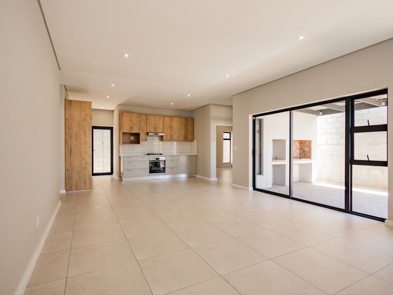 Spacious open-plan living and kitchen area featuring modern cabinetry, integrated appliances, and large sliding doors opening to an outdoor patio with a built-in braai.