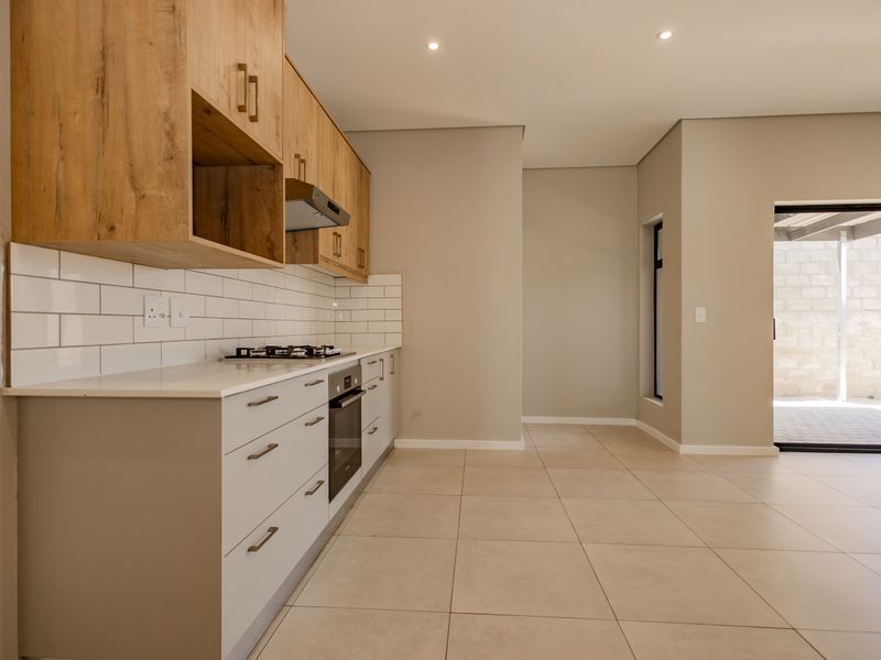 Modern kitchen featuring light wood and white cabinetry, stone countertops, subway tile backsplash, and integrated gas hob and oven, with direct access to the patio.