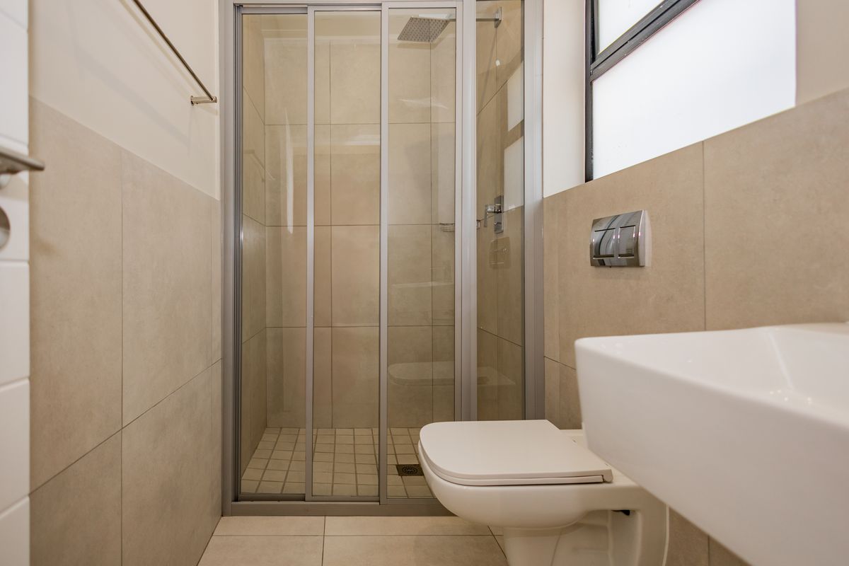 A modern, clean bathroom featuring a glass-enclosed shower with a rain shower head, wall-mounted toilet, and a contemporary basin with neutral tiling.