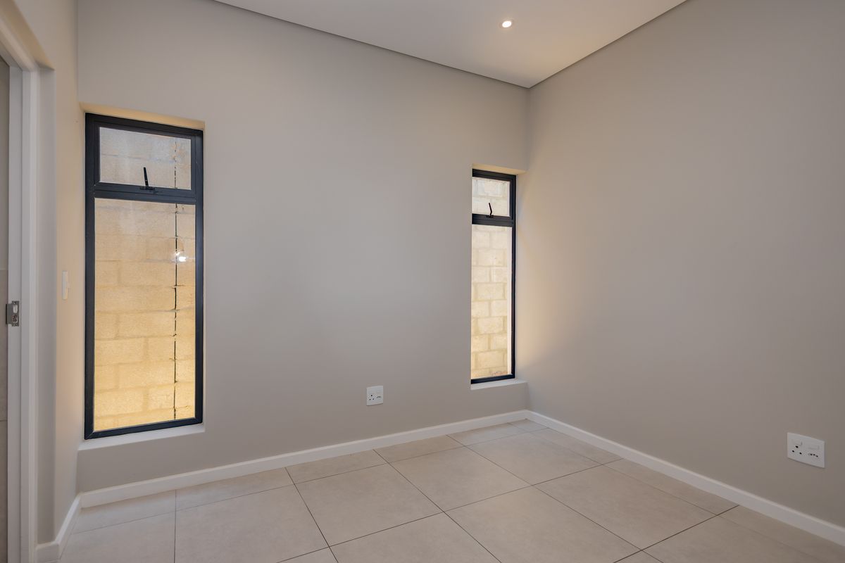 A clean, empty bedroom featuring neutral wall tones, tiled flooring, and modern aluminium-framed windows, providing a versatile space ready for personalization.