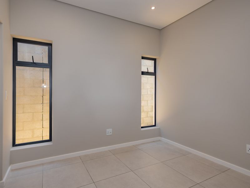 A clean, empty bedroom featuring neutral wall tones, tiled flooring, and modern aluminium-framed windows, providing a versatile space ready for personalization.