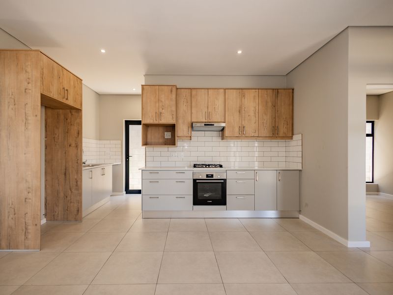 Modern kitchen featuring light wood-look cabinetry, subway tile backsplash, built-in oven, gas hob, and neutral tiled flooring in an open-plan layout.