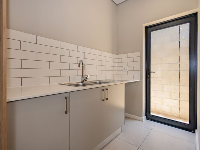 A clean and modern scullery featuring built-in cabinetry, a double bowl stainless steel sink, subway tile backsplash, and direct access to an outdoor area.