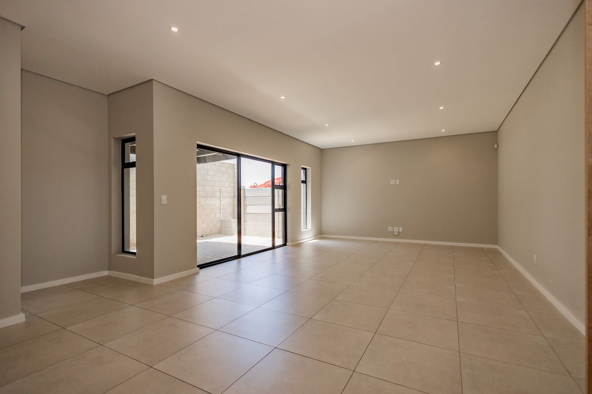 A spacious, modern, and empty living area featuring neutral tiled flooring, recessed lighting, and large sliding glass doors leading to an outdoor patio.