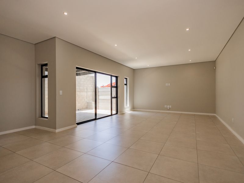 A spacious, modern, and empty living area featuring neutral tiled flooring, recessed lighting, and large sliding glass doors leading to an outdoor patio.