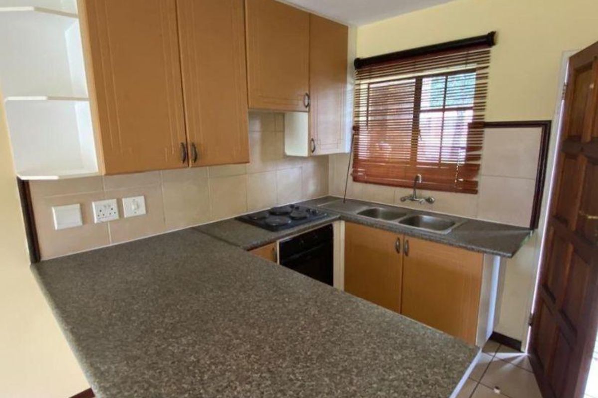 A functional kitchen featuring laminate cabinetry, stone-look countertops, a double bowl sink, and built-in cooking appliances with tiled backsplash and flooring.