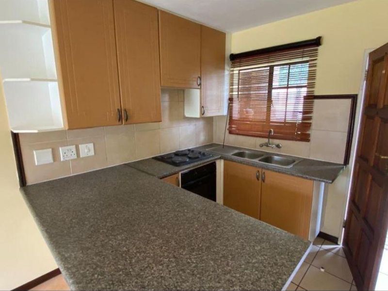A functional kitchen featuring laminate cabinetry, stone-look countertops, a double bowl sink, and built-in cooking appliances with tiled backsplash and flooring.