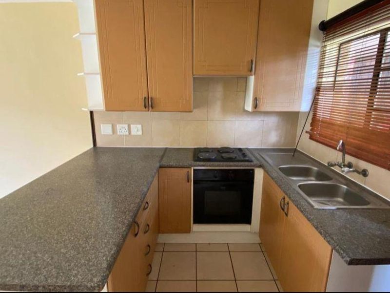 A functional kitchen featuring laminate cabinetry, a built-in oven with electric hob, double stainless steel sink, and tiled backsplash.