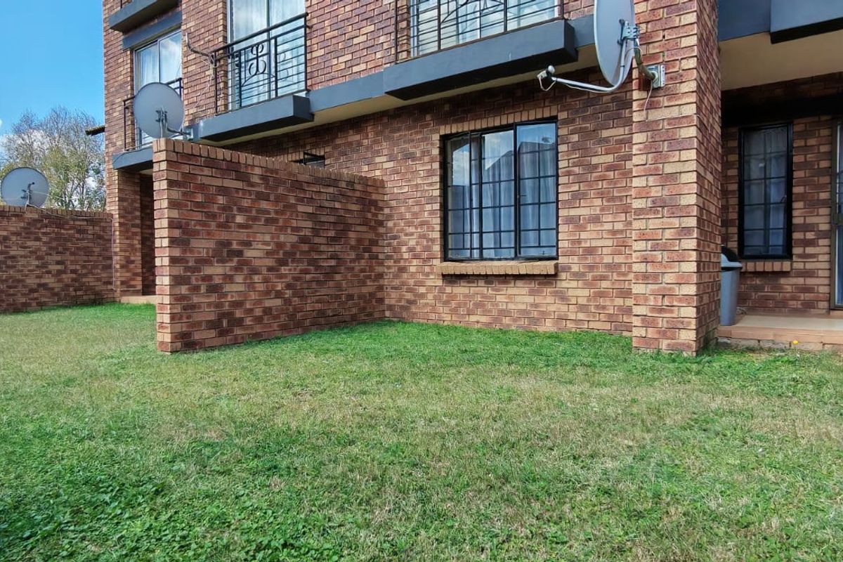 Rear view of a face brick apartment building featuring a private lawn area, security bars on windows, and sliding door access.