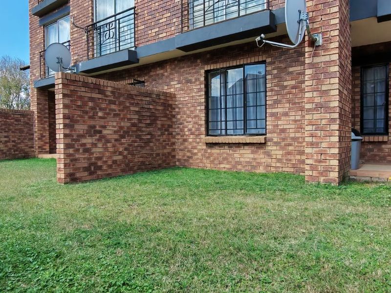 Rear view of a face brick apartment building featuring a private lawn area, security bars on windows, and sliding door access.