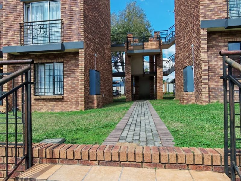 Exterior view of a face brick apartment complex featuring paved walkways, external staircases, and wrought iron balcony railings.