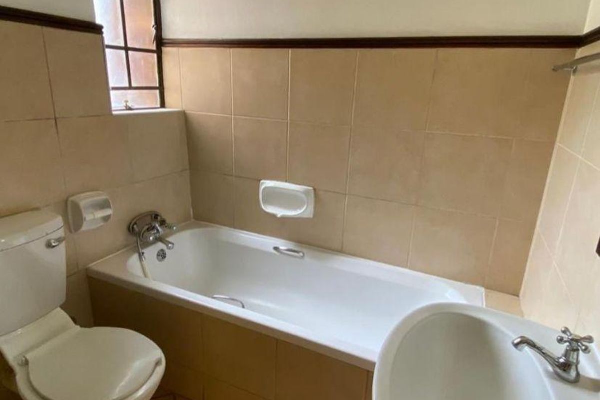 A functional bathroom featuring a standard bathtub, pedestal basin, and toilet with neutral ceramic wall tiling.