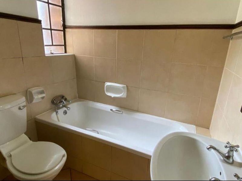 A functional bathroom featuring a standard bathtub, pedestal basin, and toilet with neutral ceramic wall tiling.