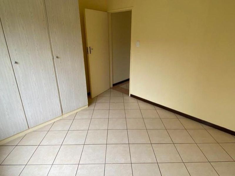 An empty bedroom featuring neutral tiled flooring and built-in cupboards, offering a blank canvas for personalization.