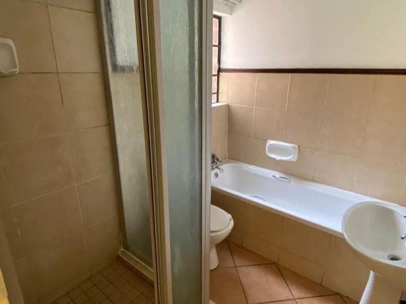 A functional bathroom featuring a shower enclosure, bathtub, pedestal basin, and toilet with neutral ceramic wall and floor tiling.