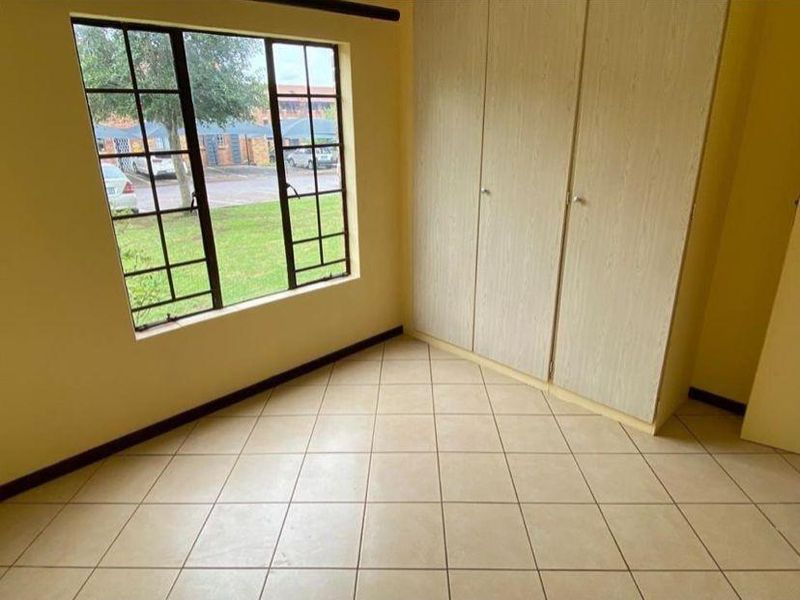 A bright, empty bedroom featuring neutral tiled flooring and built-in wooden cupboards, offering a clean and versatile space.
