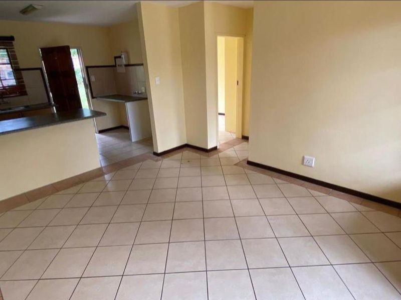 An open-plan living and kitchen area featuring tiled flooring, neutral walls, and a functional kitchen layout with a breakfast bar.