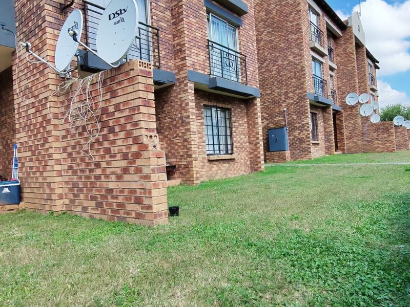 Rear view of a multi-story face brick apartment complex featuring private garden spaces, metal security fixtures, and multiple satellite dish installations.