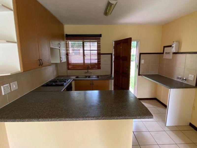 A functional kitchen featuring laminate cabinetry, built-in hob, double basin sink, and tiled flooring, offering a practical layout with direct outdoor access.