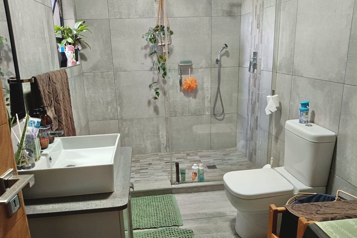 Modern bathroom featuring a walk-in shower with glass screen, vanity basin with storage cabinet, and a contemporary toilet with grey tiled finishes.