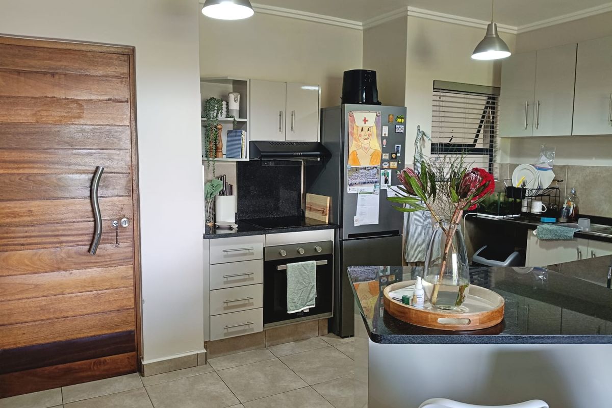Modern kitchen featuring granite countertops, built-in oven and hob, extractor fan, and ample cabinetry, complemented by tiled flooring and pendant lighting.