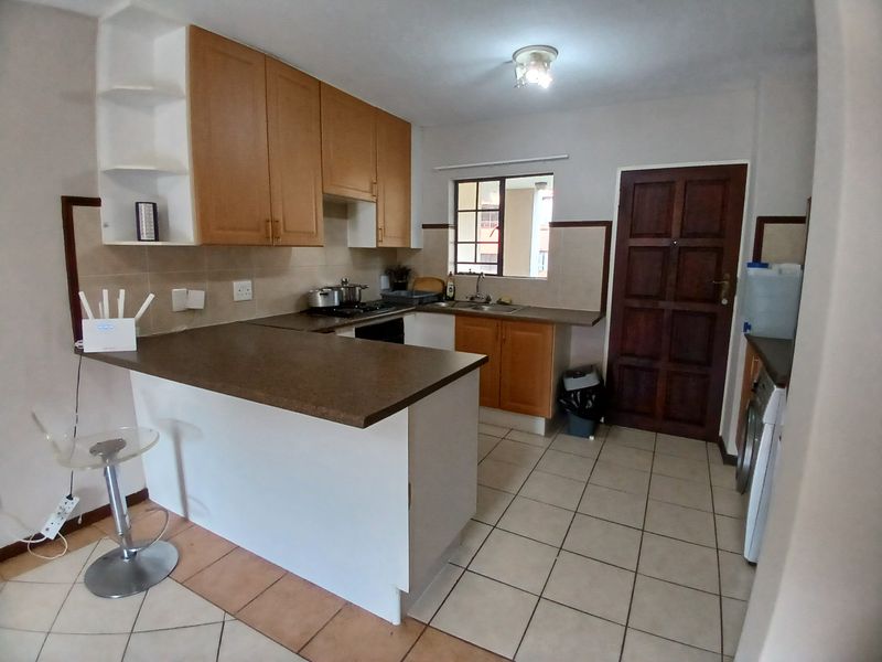 Functional kitchen featuring laminate cabinetry, tiled backsplash, double basin sink, and a breakfast counter, with ceramic floor tiles throughout.