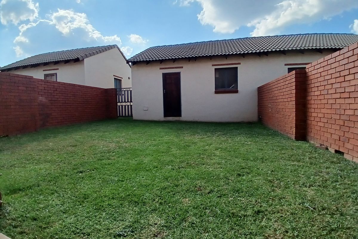 A private rear garden area featuring a well-maintained lawn, enclosed by sturdy brick boundary walls and accessible via a metal gate.