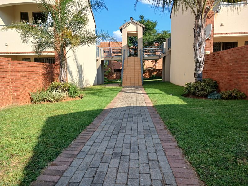 A well-maintained communal garden area featuring a paved walkway, brick boundary walls, and a central staircase connecting apartment building sections.