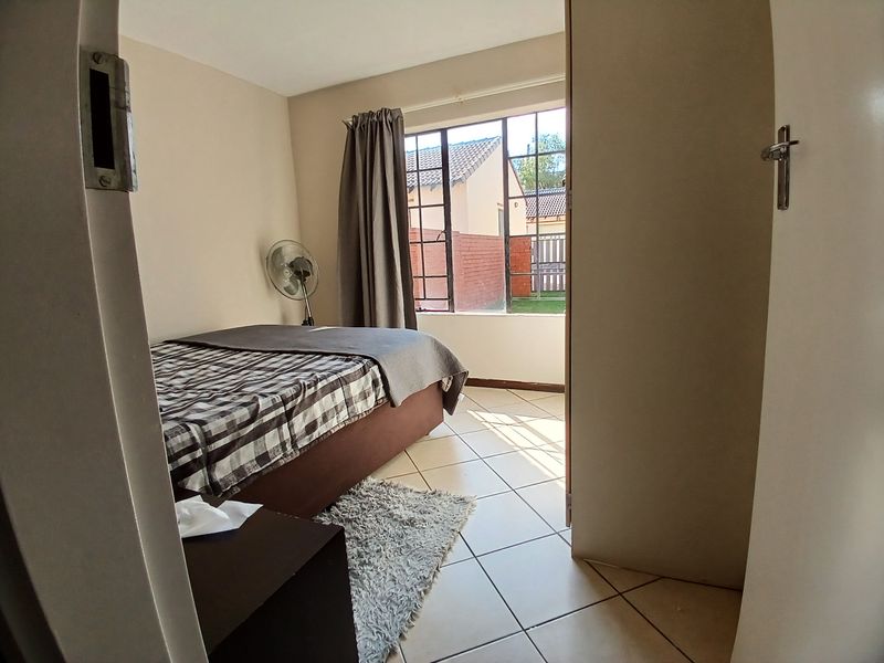 A functional bedroom featuring tiled flooring and a steel-framed window, offering a view of the exterior property grounds.