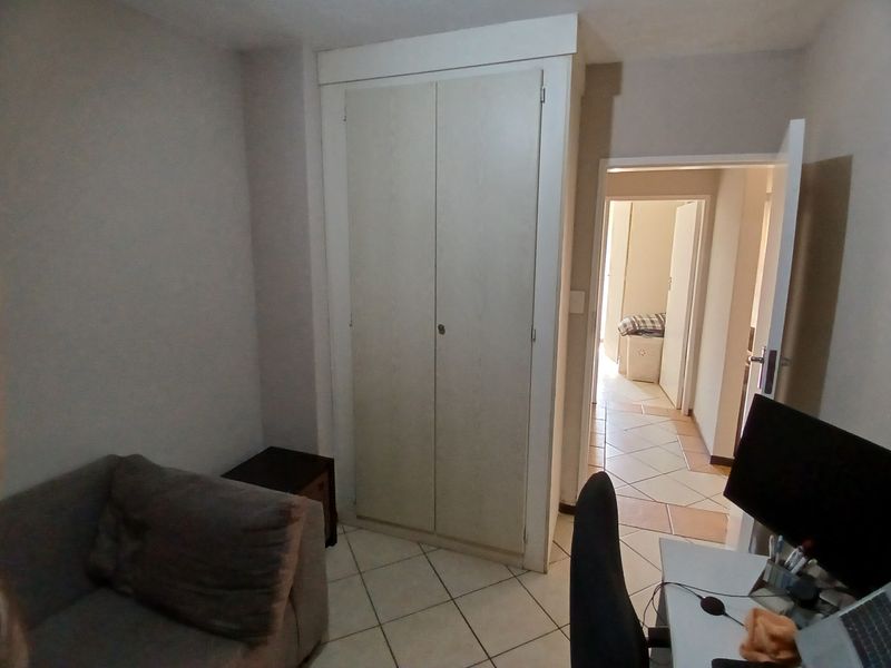A bedroom featuring tiled flooring and a built-in wardrobe, with a doorway leading to an adjacent hallway.
