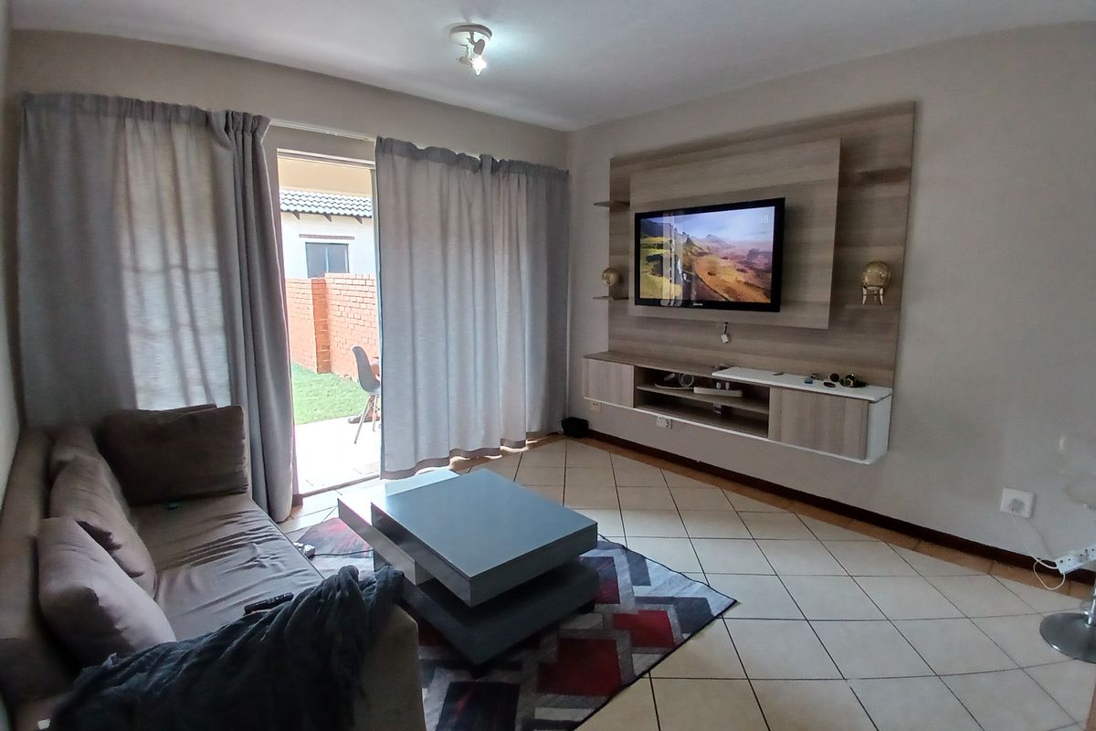 A comfortable living room featuring a built-in media unit, tiled flooring, and direct access to an outdoor patio area through sliding glass doors.