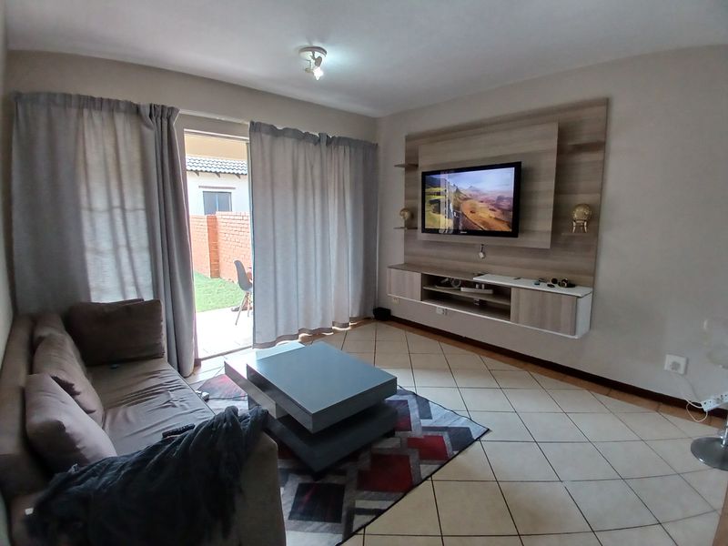 A comfortable living room featuring a built-in media unit, tiled flooring, and direct access to an outdoor patio area through sliding glass doors.