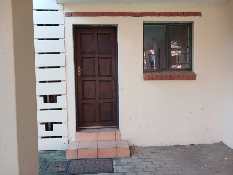 Entrance area featuring a timber panel door, brick detailing, and tiled step leading to a paved exterior space.