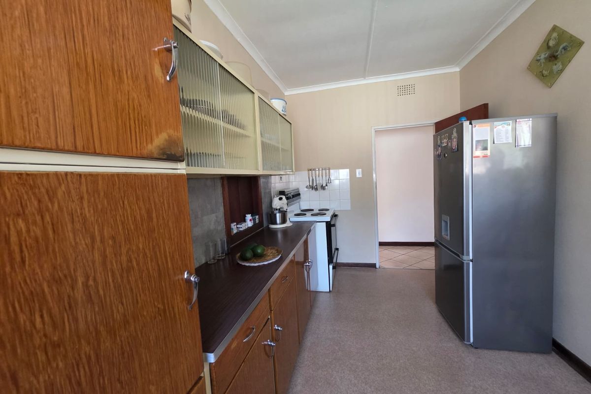 A dated kitchen featuring wood-look cabinetry, laminate countertops, and tiled splashbacks, providing a functional layout with space for a freestanding stove and refrigerator.