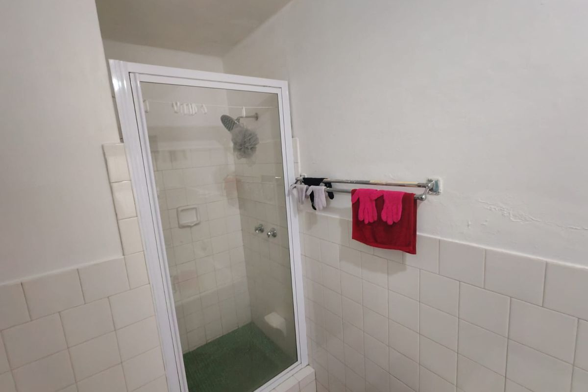 A functional bathroom featuring a shower enclosure with tiled walls and a wall-mounted towel rail, requiring some cosmetic maintenance to the wall surfaces.