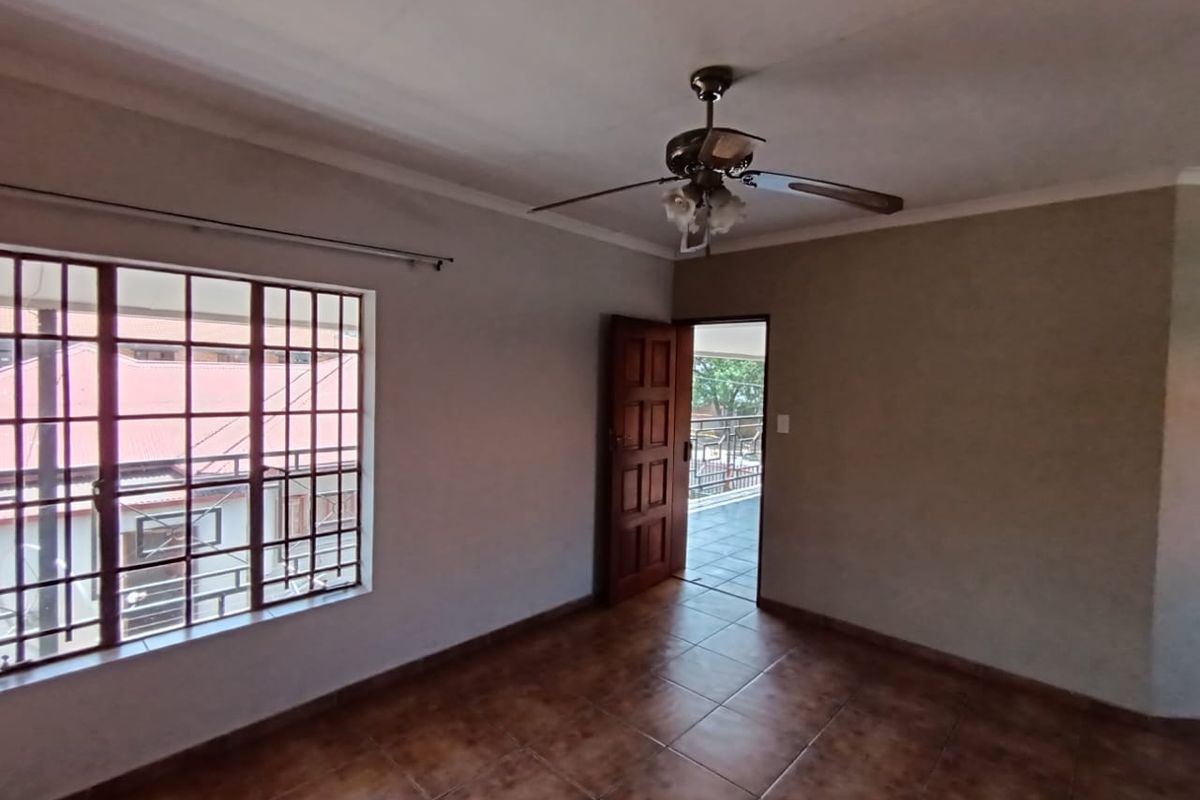 An empty bedroom featuring tiled flooring, a ceiling fan, and a timber door leading to an outdoor balcony area.