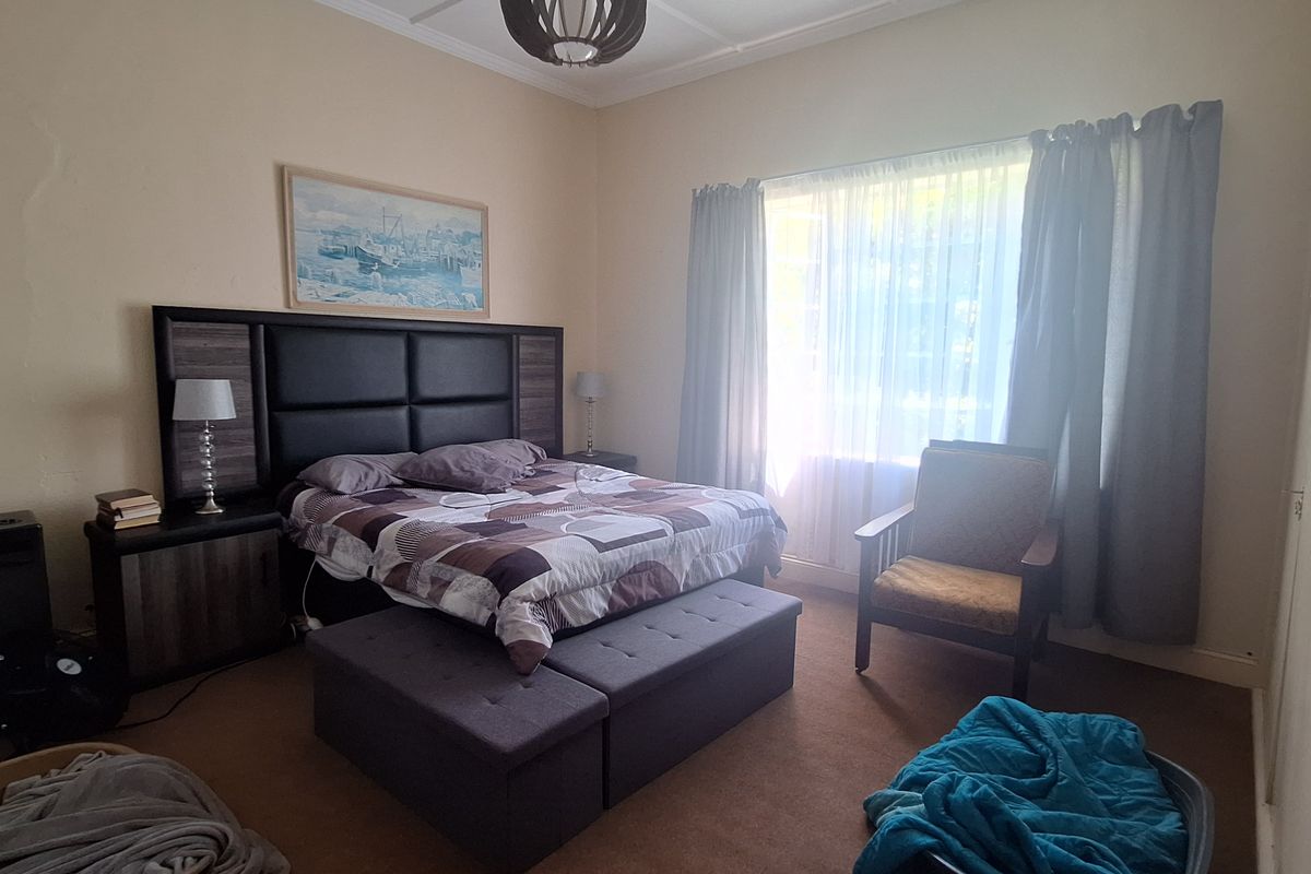 A spacious bedroom featuring high ceilings with decorative molding, large window with natural light, and neutral wall finishes.