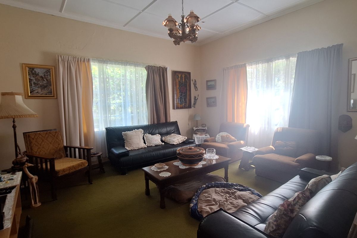 A spacious living room featuring traditional ceiling tiles, large windows with natural light, and wall-to-wall carpeting.