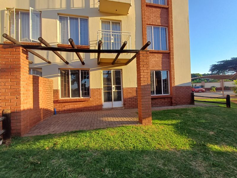 Rear view of the apartment building featuring a paved patio area with a timber pergola, brick facade, and access to a private balcony.